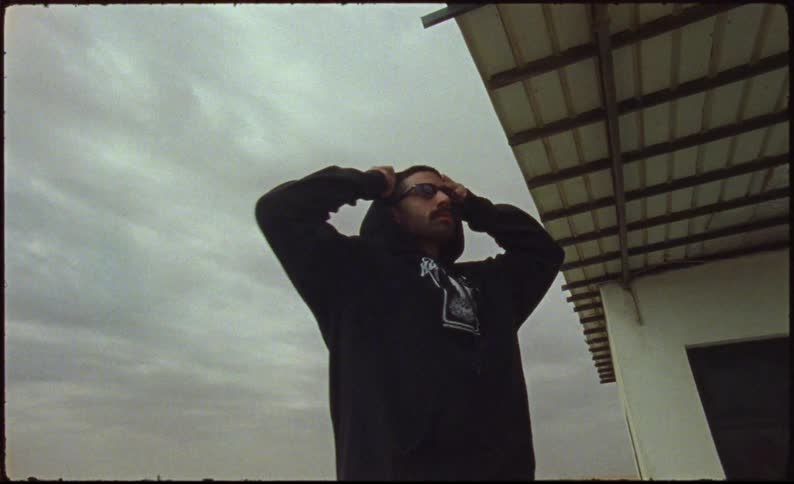 Man in a sweatshirt and sunglasses in a deserted environment next to a house