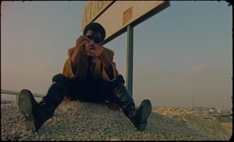 A young man sits over a mound of gravel playing with a small chain next to a weathered sign