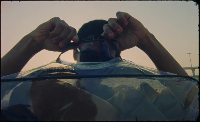Teenager holding a transparent suitcase in an outdoor environment with a highway in the background in the late afternoon