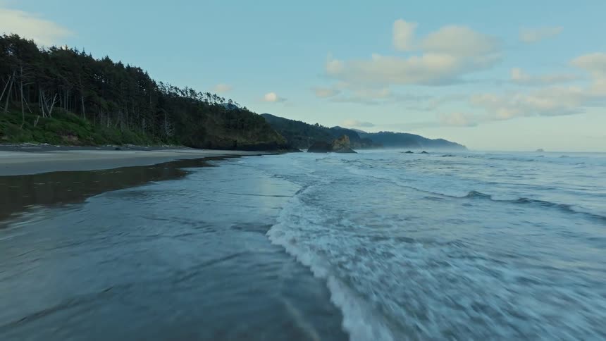 Aerial view of a coastal scene with gentle waves and a sandy beach under a partly cloudy sky