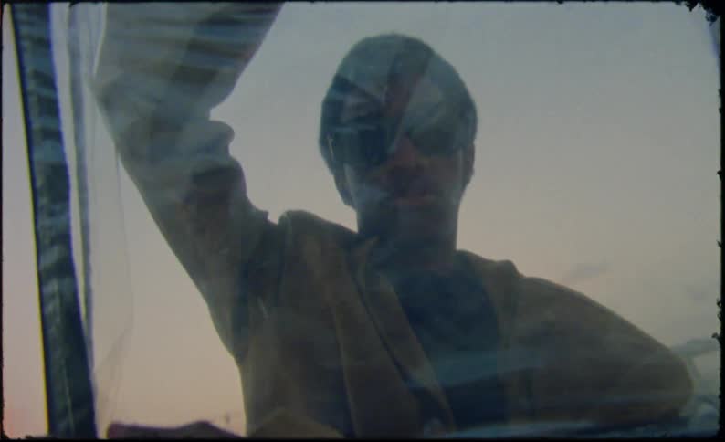 A young man stands holding up a translucent bag with visible traffic on a bridge behind him