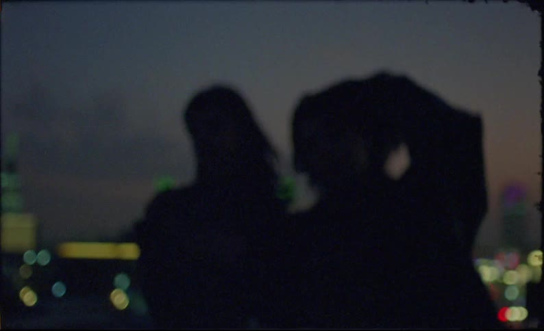 Silhouette of two women embracing on the terrace of a building overlooking buildings in a metropolis at night