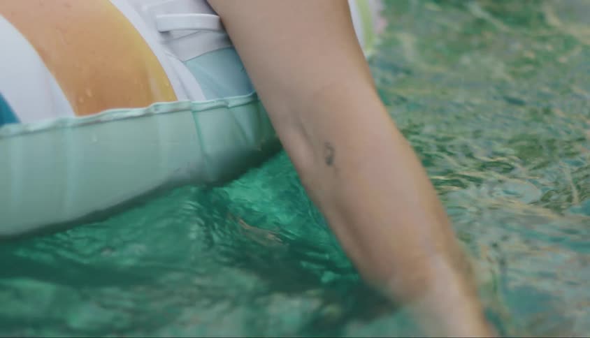 Person on a float with their hand passing through the waters of a pool