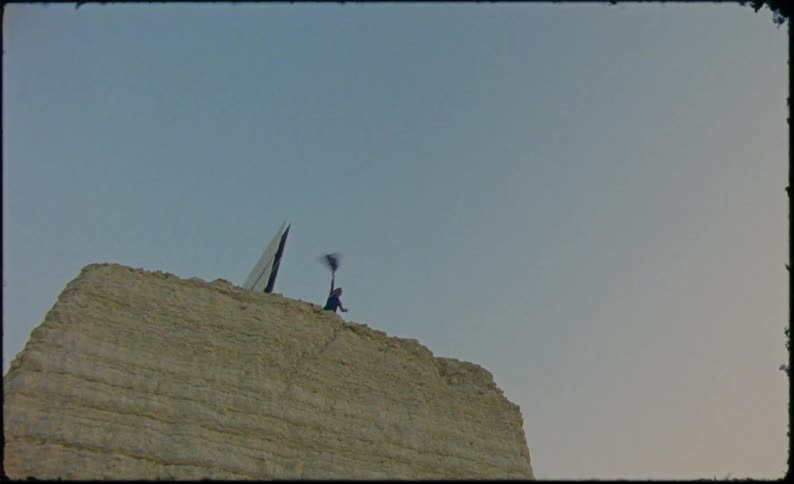 Person on top of a hill throwing clothes into the air that fall to the ground