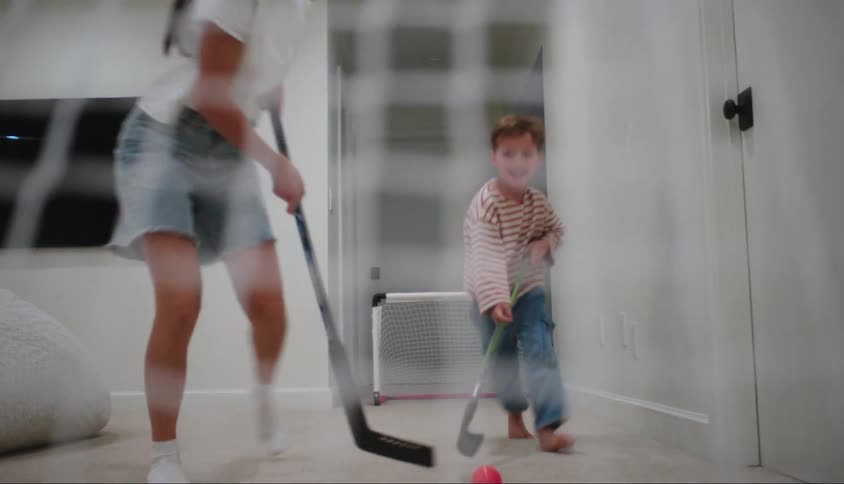 Two children playing hockey among themselves in a room inside the house