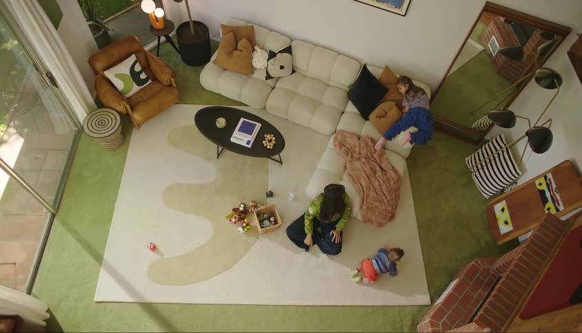 Mother in a room with a girl climbing on the sofa and a baby crawling