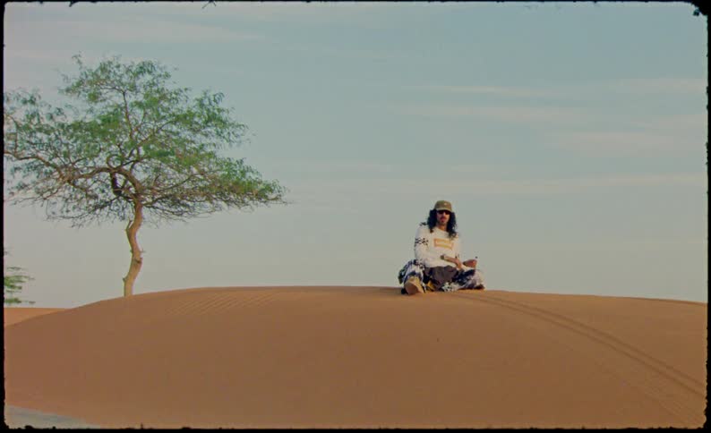 Man holding a scarf sitting on a desert dune