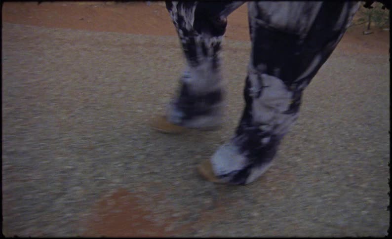A man strides across the desert with towels and rugs slung over his shoulder as he follows a worn path