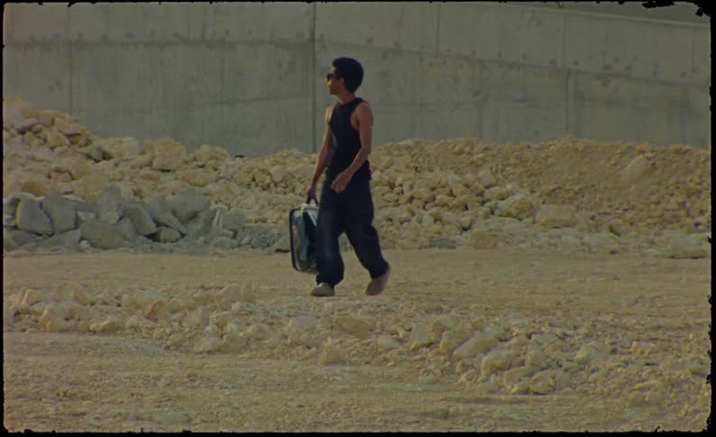 A young man carrying a transparent suitcase walks through a construction site