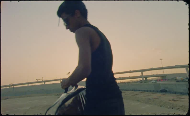 A young man drops a transparent suitcase in the middle of a construction site at sunset