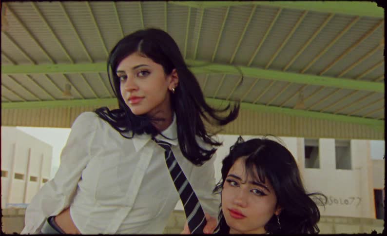 Two girls wearing schoolgirl uniforms playing with a shopping cart on an abandoned lot