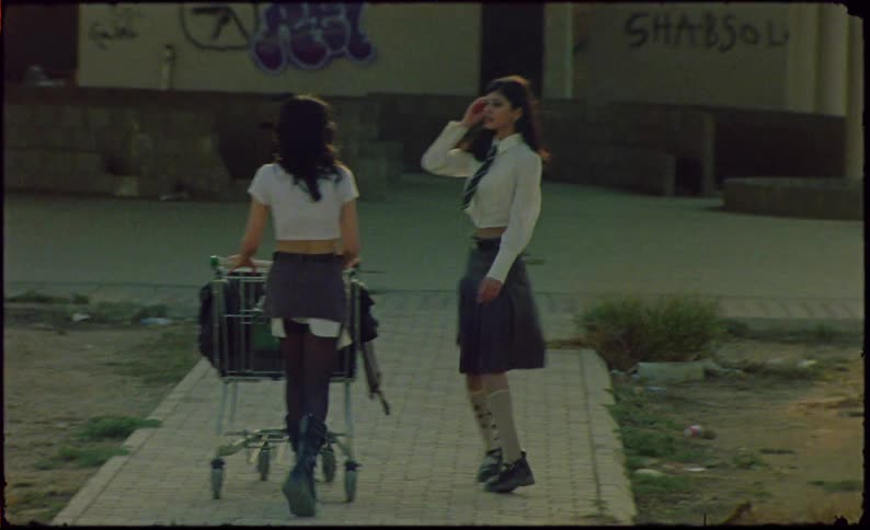 Two young women dressed in college clothes walking with a shopping cart in an abandoned environment with graffiti