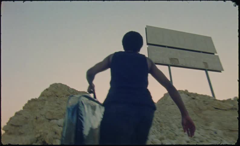 Man with a transparent bag with clothes inside climbing a rocky hill with a sunset on the horizon