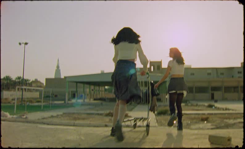 Two girls wearing schoolgirl uniforms playing with a shopping cart on an abandoned lot