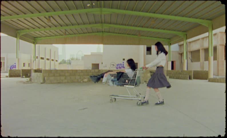 Two young women in college clothes playing with a shopping cart in an abandoned environment