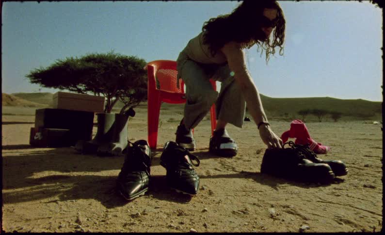 Woman sitting on a chair in the desert picking up a pair of shoes in front of her