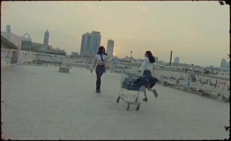 Two girls wearing schoolgirl uniforms playing with a shopping cart on an abandoned building