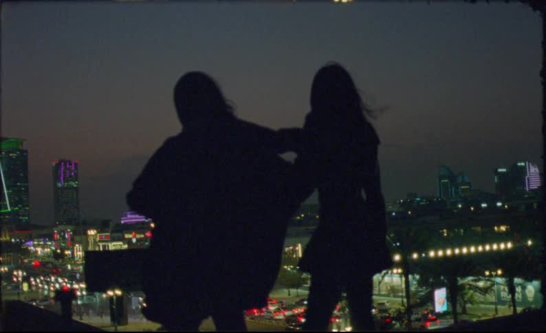 The women are swaying back and forth while holding looking out over the night lights of the city