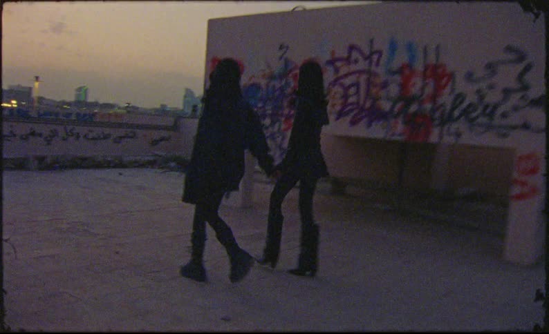 Two female models holding hands walking on the terrace of a building
