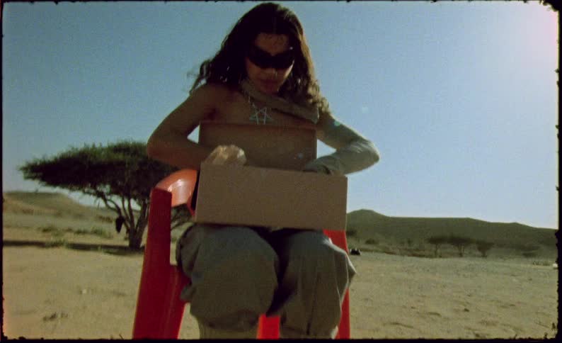 Woman with a shoebox sitting on an orange chair in the middle of the desert