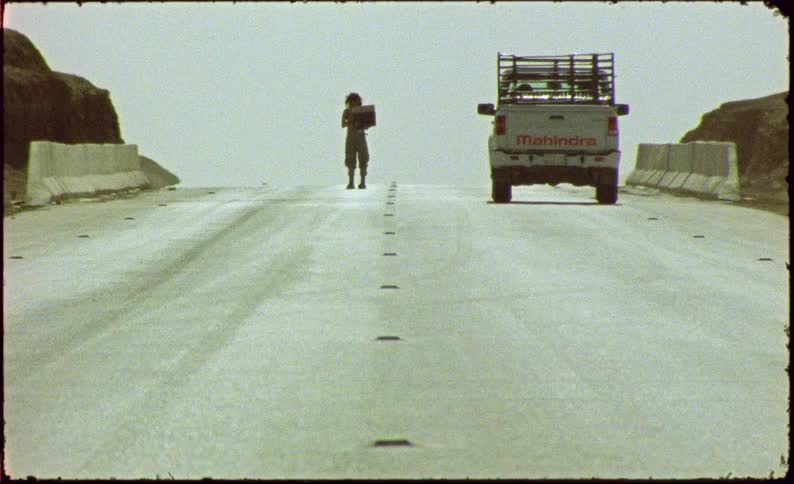 White pickup truck traveling down a street and a woman approaching it