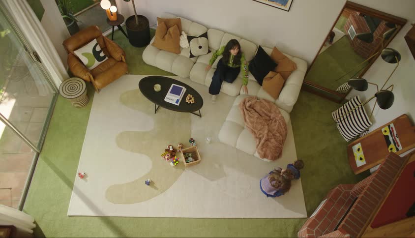 Mother sitting on the sofa with her daughter and a baby crawling across the carpet