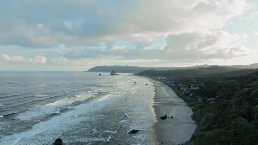 Waves roll onto the beach passing rock outcroppings as they approach the homes in a coastal town