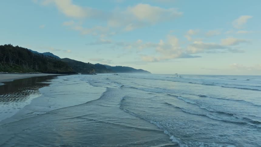 A beach with small waves going to the coast and there is a mountain on the left side