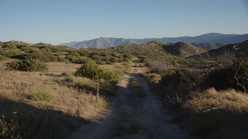 A rough dirt road runs through grasslands in a rural area