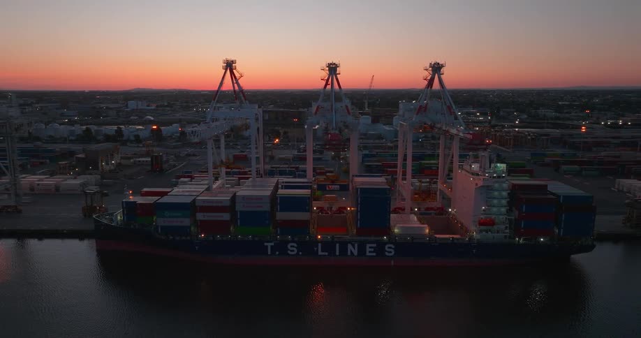 A ship filled with cargo containers sits in a river next to a port