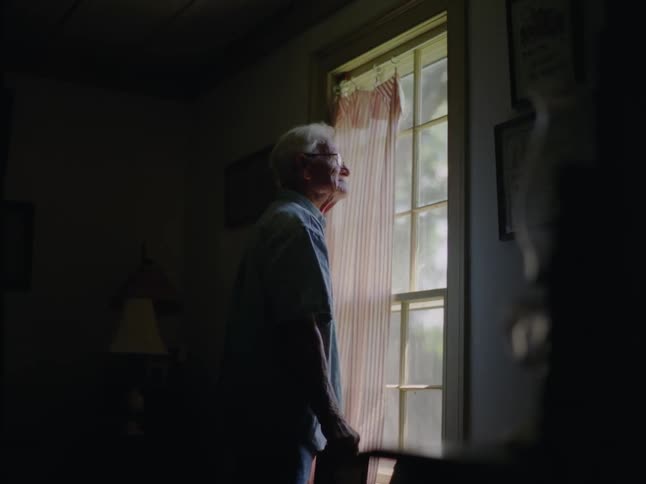 An elderly man looking out a window