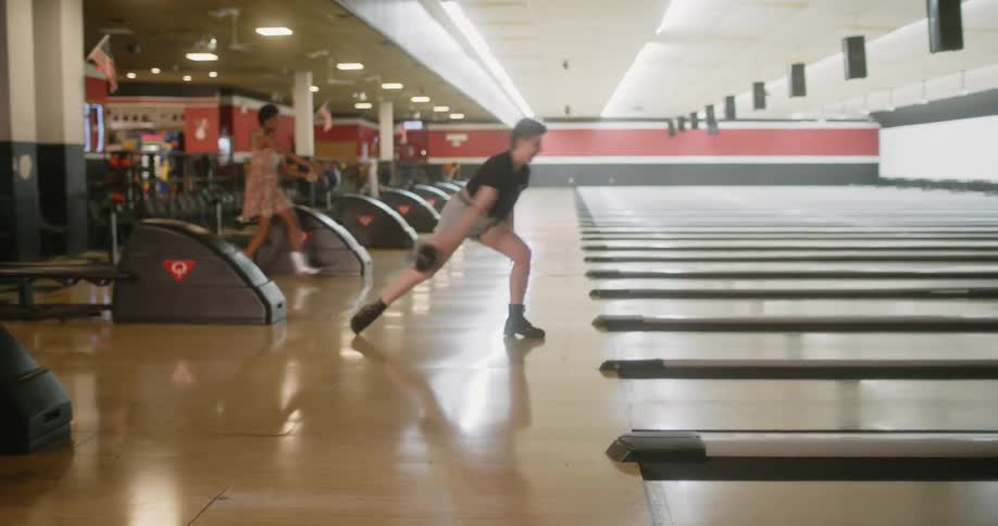 The man in the jeans bowls thena few lanes down the woman in the shorts bowlsthen finally the black lady in the dress bowls at the end and she celebrates