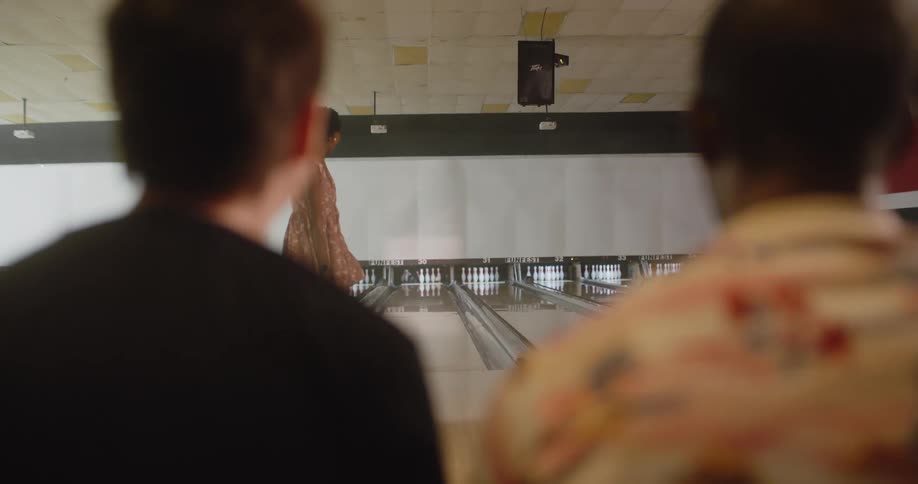 A woman in yellow dress and is throwing a bowling ball and hits the pins and two people in front of her celebrate