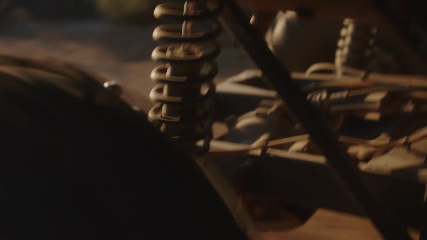 A tire of a vehicle driving on a dirt road and there is a suspension spring next to the tire