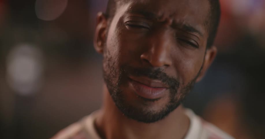 The black man with the beard is shaking his head and looks upsethe says something while looking at the camera