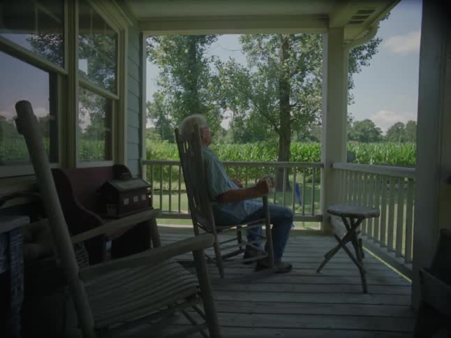 Elderly man sitting on chair in a backyard observing the landscape