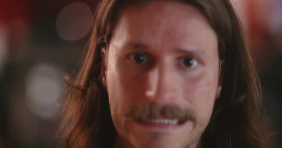 A long haired man raises his head and cringes