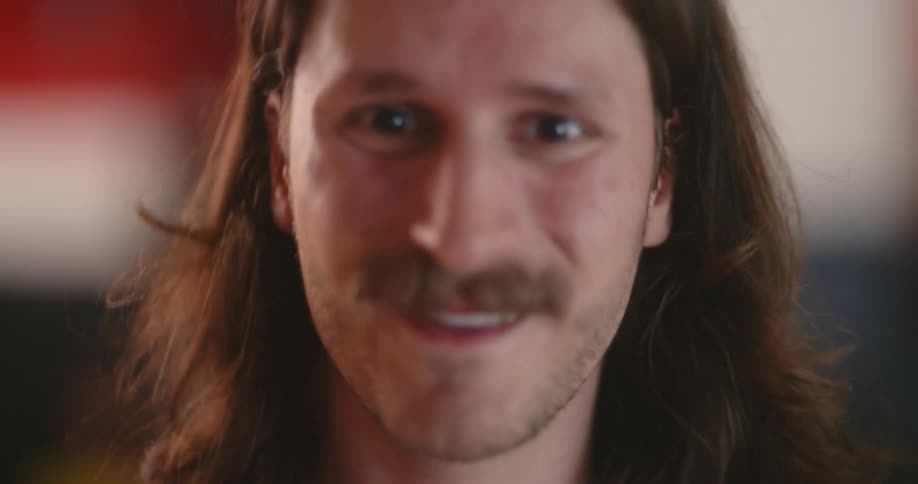 A long haired man raises his head smiles and speaks