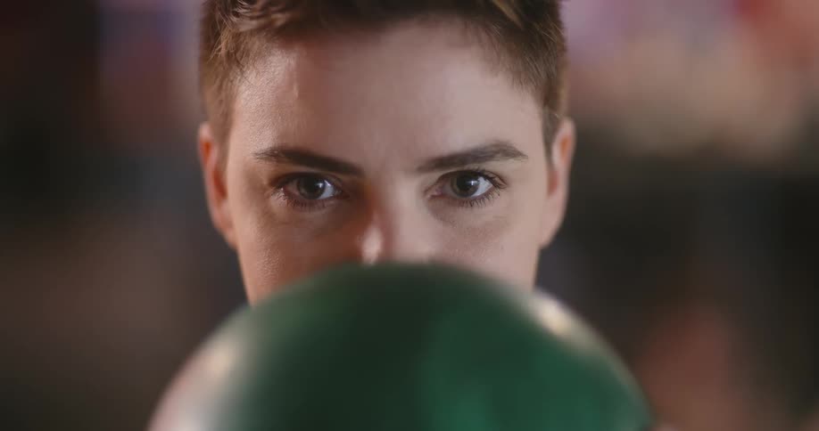 A woman with short hair holds a bowling ball up to cover the lower part of her face