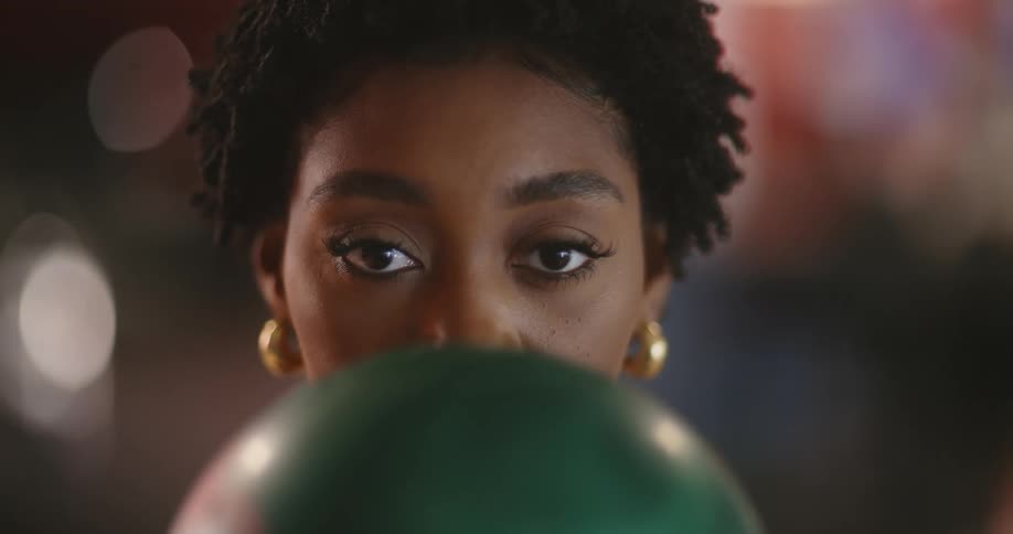 The face of a young woman with golden earrings and she is holding a green ball and looking straight ahead