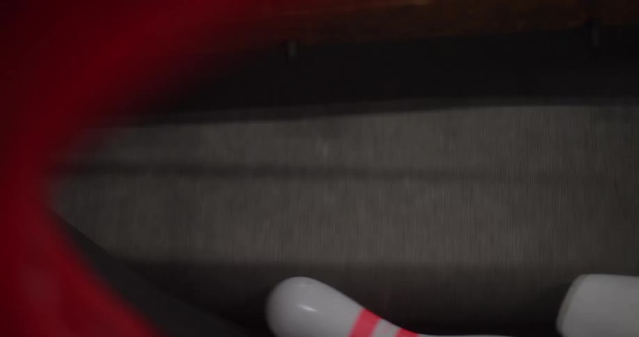 The bowling pins are spinning inside of a red machine with a black belt inside that is moving