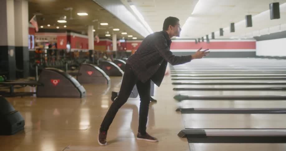The man in black bowls and watches till he sees what happens then he walks back to the grouptghe long haired man behind him bowls and is excited as he walks back to his group