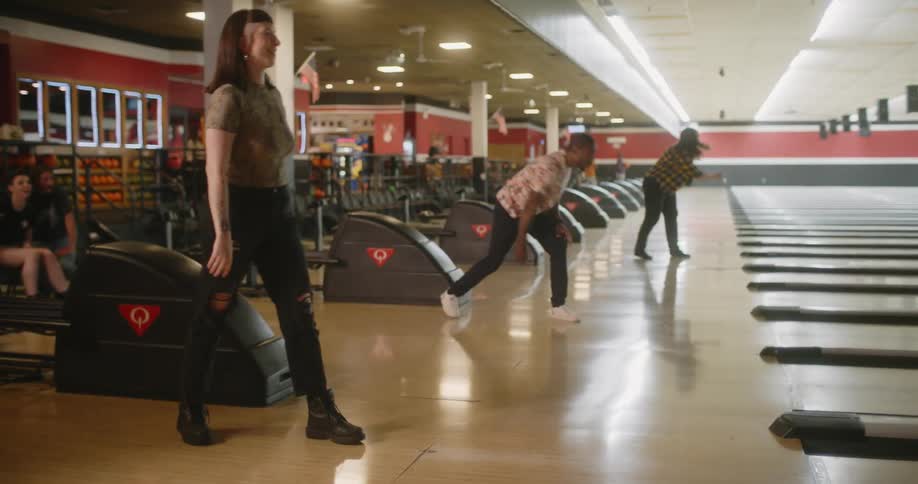 A woman is throwing a bowling ball on a lane with a wooden floor and then she celebrates