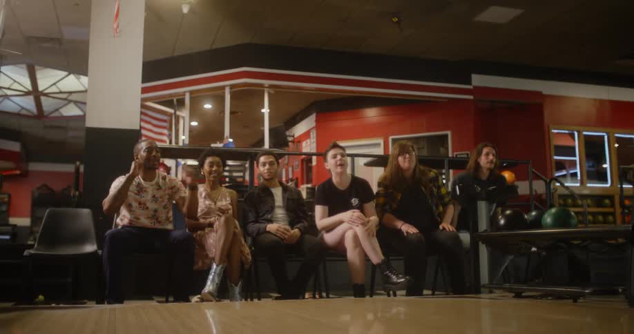 A woman standing with a bowling ball ready to throw it and some of her friends behind her are encouraging her