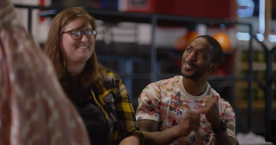 Two friends sitting in a bowling alley celebrate as another joins them