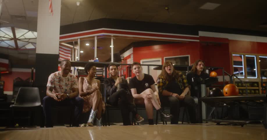 The woman throws the bowling ball while the group watches she then walks back towards the group