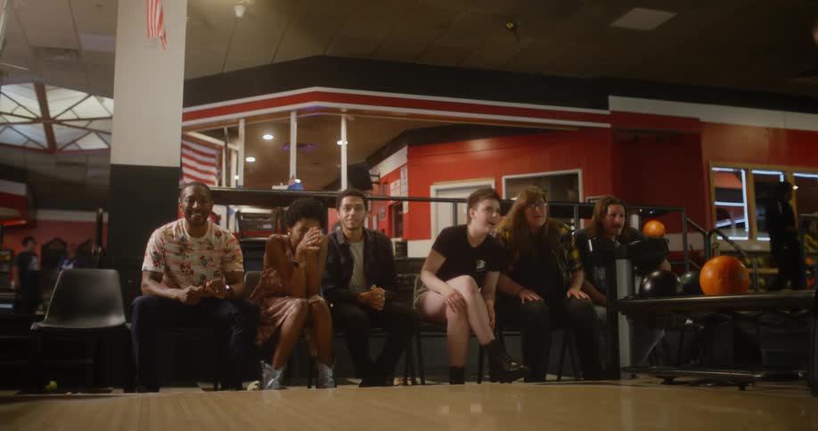 Woman throwing a bowling ball and then cheering with her friends who are sitting in the background
