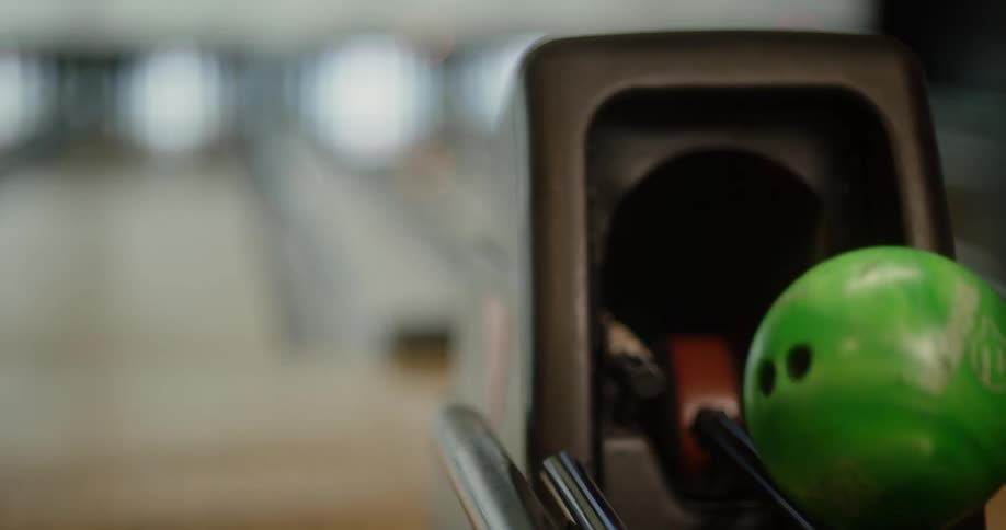 Man hand catching a green bowling ball from a machine on a court