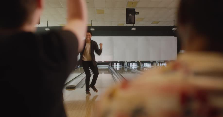 The man in black throws the bowling ball and turns to celebrate with the people who are cheering him on