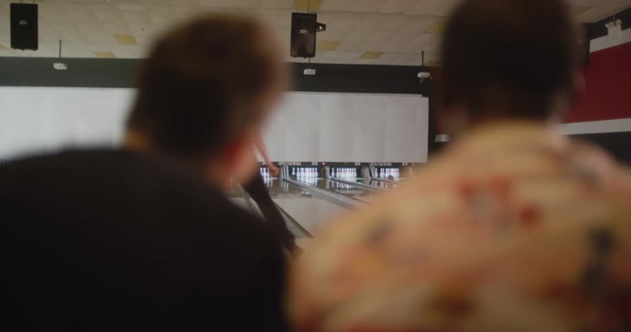 The woman throws the bowling ball and gets a strikeshe turns around to the men and dances on her way to her seat